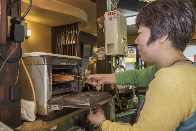 ドッグパンにウインナーとキャベツをはさみ、年季の入った電気オーブンの焼き具合を巧みに調節して作る。