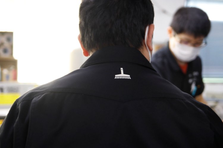 黒色のシックなオリジナルユニフォームの襟元には、特殊製本に欠かせない刷毛のワンポイントが。