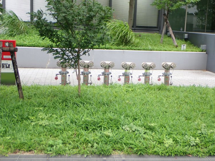 植え込みの向こうに横一列に並ぶ自立型の送水口。