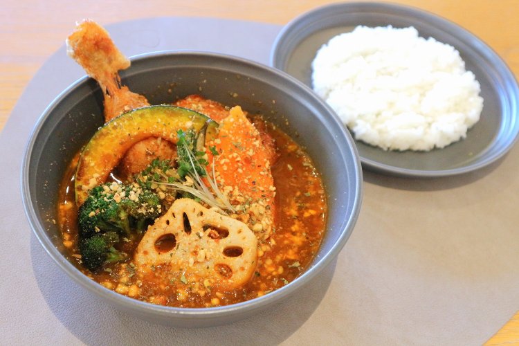 写真は、骨付きチキンと7種の野菜カリー1230円の濃厚トマトスープ。こくまろココナッツスープも選べる。