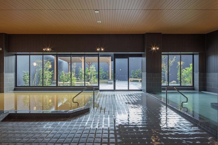 左側が源泉風呂の下段、右側は白湯の浴槽。ガラス窓の向こうに露天風呂が見える。