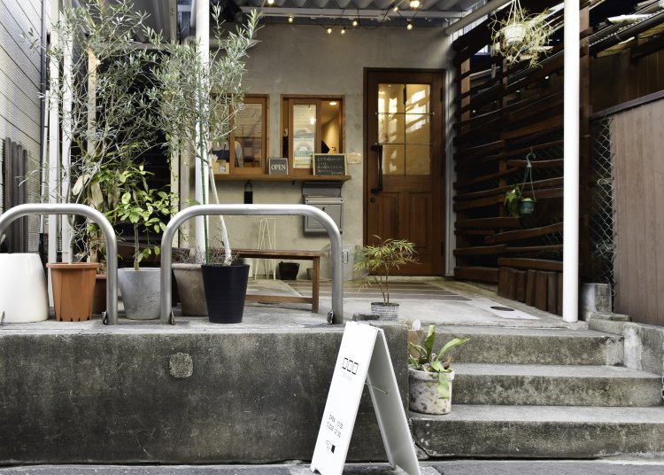 住宅と住宅に挟まれた奥まった作り。テイクアウトが注文できる窓が。店頭にはベンチがあり、ここでラテをいただける。