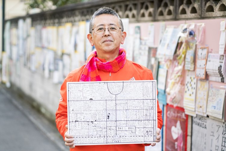 「あっおやまっぷ」を手にする青山さん。『楽風』の塀は街やアートに関する情報もずらりと貼られ圧巻。カードやチラシははがして持ち帰れる。