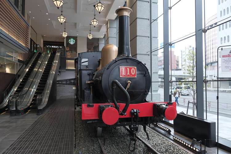 新南口直結「CIAL桜木町ANNEX」は2階まで吹き抜けのビル内に青梅鉄道公園から移設された110形蒸気機関車を展示。掃除の行き届いた室内に展示され、行き交う人々に興味を持たれて110形も幸せそう。