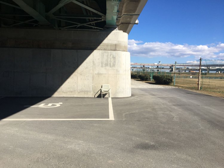 広い駐車場にぽつねんと、白い野良イス。