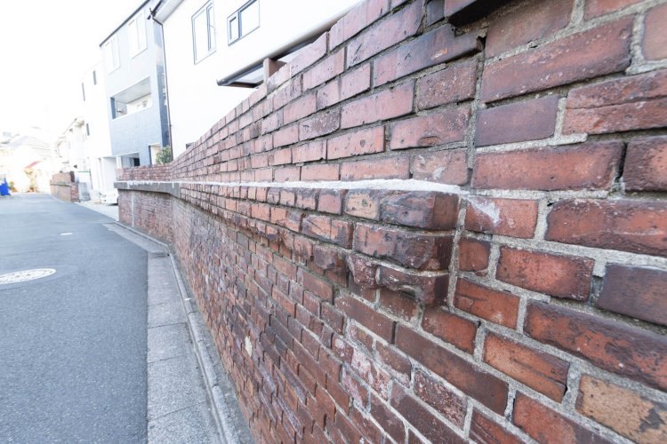 ［街に遺構あり！］ 園の外に続く古いレンガ塀は、大正時代の遊園地の敷地の名残。宅地となってからは家の境界や盛り土の土留めとして利用された。現在は歴史的遺構として保存されている。