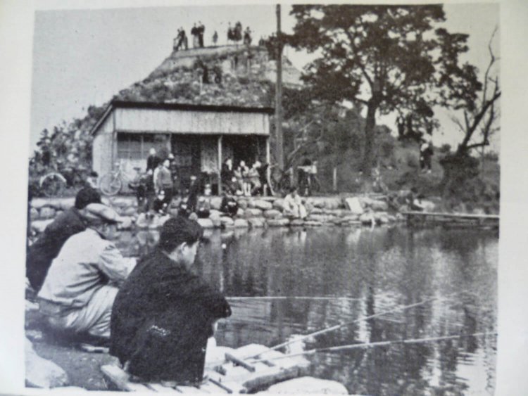 ［1950年ごろ］ オープンしたばかりの釣り堀の様子。家族を連れてきたお父さんたちだろうか、大人たちでにぎわっている。奥には現在はない山が。