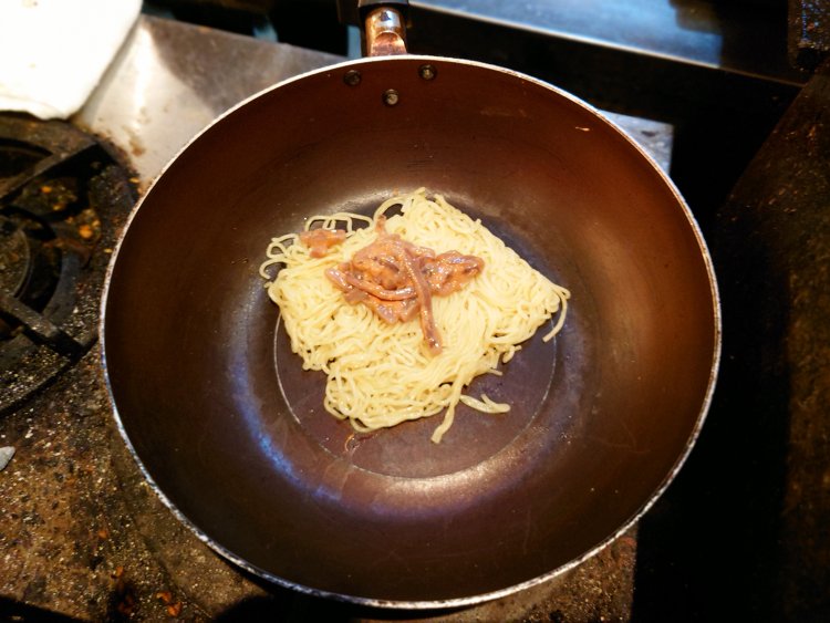生麺をレンジで温めてから鍋に、その上に塩辛をのせて炒めていく。