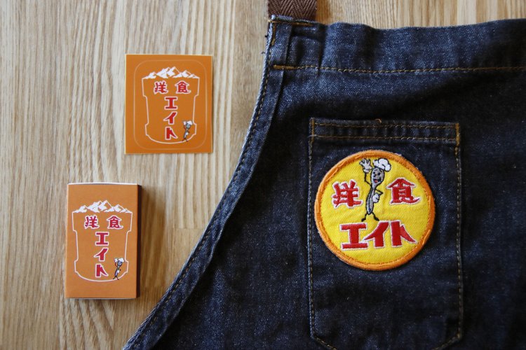 エプロンのワッペンにマスコットのエイトくんが。マッチやステッカーはおみやげに。