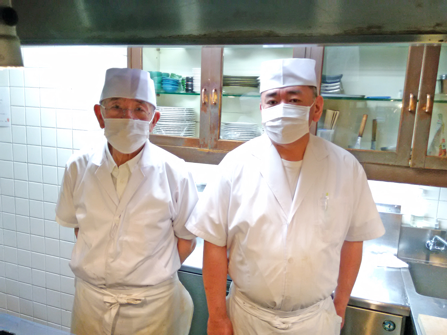 和食一筋60年以上の熟練料理人・村岡清さん（左）と、絶妙な火加減でとんかつを揚げる鈴木泰輔さん（右）。