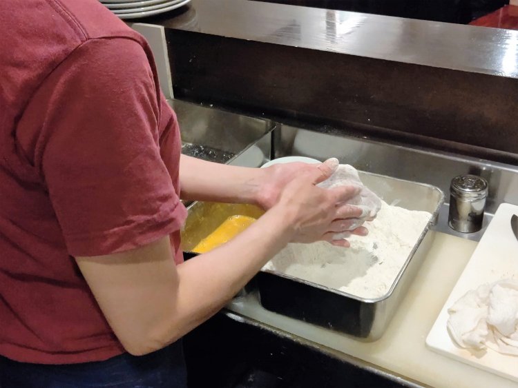 卵液に浸す前に余分な小麦粉をやさしく落とす。そうすることで衣が剝がれにくくなるという。