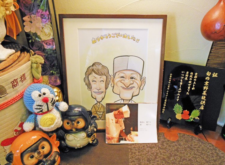 店に入ってすぐ左手の棚には、創業者・菊浦達氏の写真と、女将・美貴子夫人との似顔絵が飾られている。