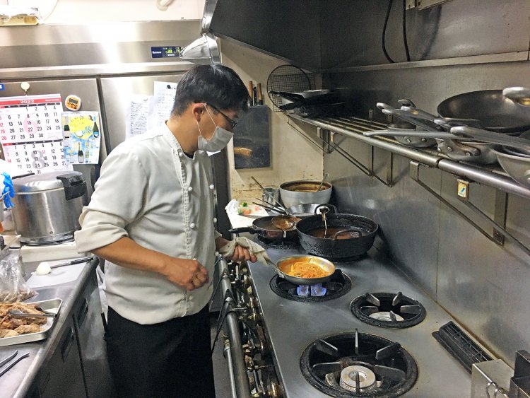 厨房でフライパンを振る木瀬シェフ。