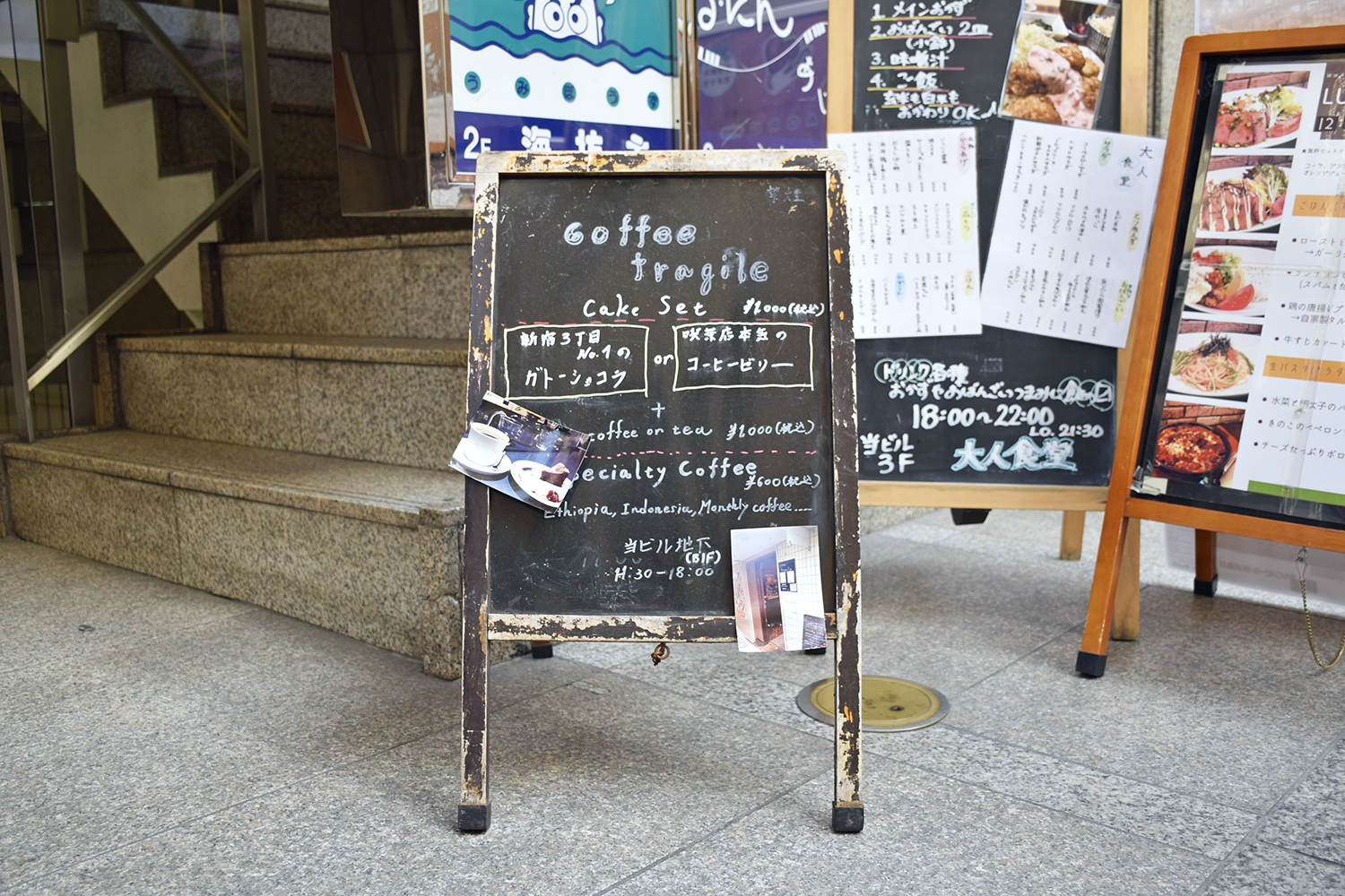 ビル入口に置かれた『coffee fragile』の立て看板。「新宿3丁目NO.1のガトーショコラ」の文字が目を引く。