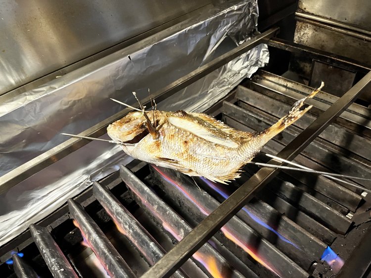 「いい真鯛だね！　これはうまいですよ」と芳賀さん。手早くさばいて塩焼きに。香ばしいかおりが店いっぱいになり期待値MAX！