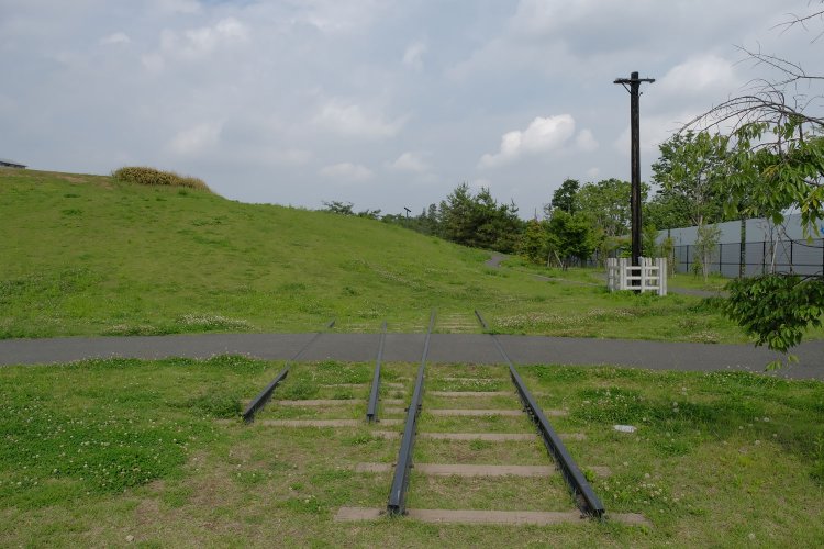公園内の芝生から現れた４本のレール。傍らには電信柱。この場所にあった引込線のレールを活用し、このようにモニュメントとして整備した。