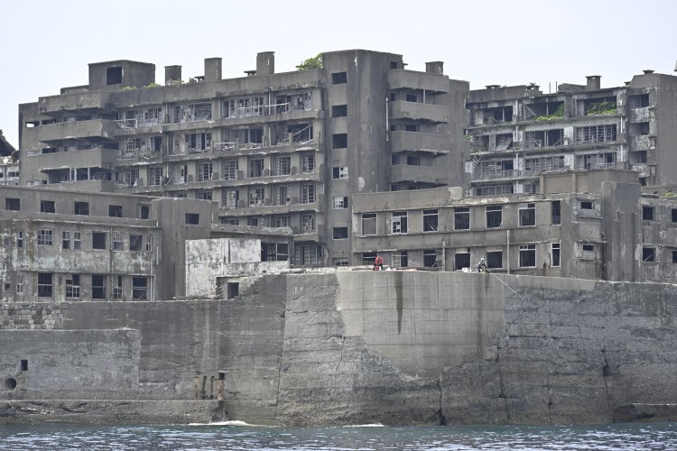 端島病院（左）と隔離病棟（右）。背後は65号棟。護岸は10ｍ近くあると思われる。それほど波が高い。釣り人がいるのはなぜだろう。（グレーな存在なのか）