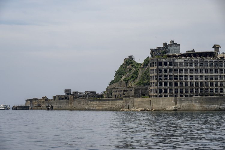 北東から見る。右が学校。選炭、貯炭場施設の廃墟群が続いている。切り立った崖が元々の端島の崖。かなり埋立拡張したのが分かる。左端に写る船のところに観光上陸用ドルフィン桟橋がある。