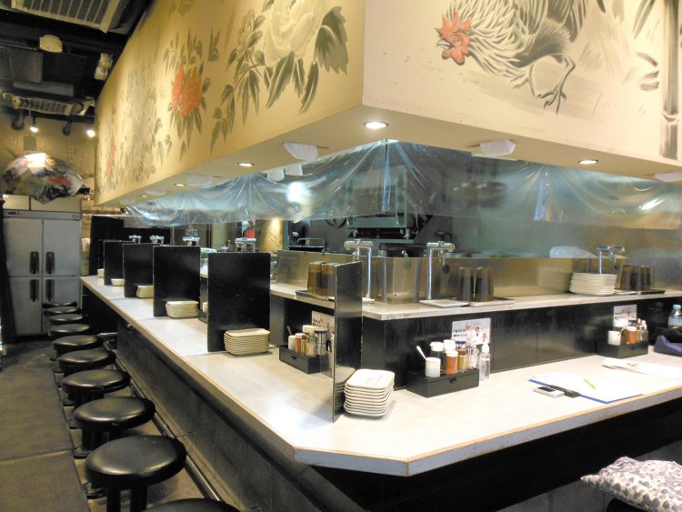 鶏の水墨画が壁面に描かれた店内。Ｌ字型のカウンターに14席ある。