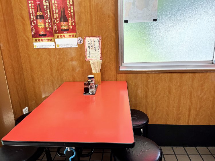 朱色のテーブルと黒の丸いパイプイスのコントラストと壁の木目がいいカンジ。