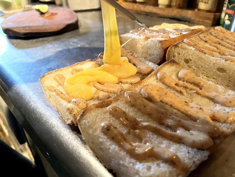 こんがり焼いたバゲットに特製マヨソース、トロトロのチーズ、自家製ピクルス、ハム、炒めたスペアリブを乗せ、ブラックペッパーをかけてさらにライムを絞る。