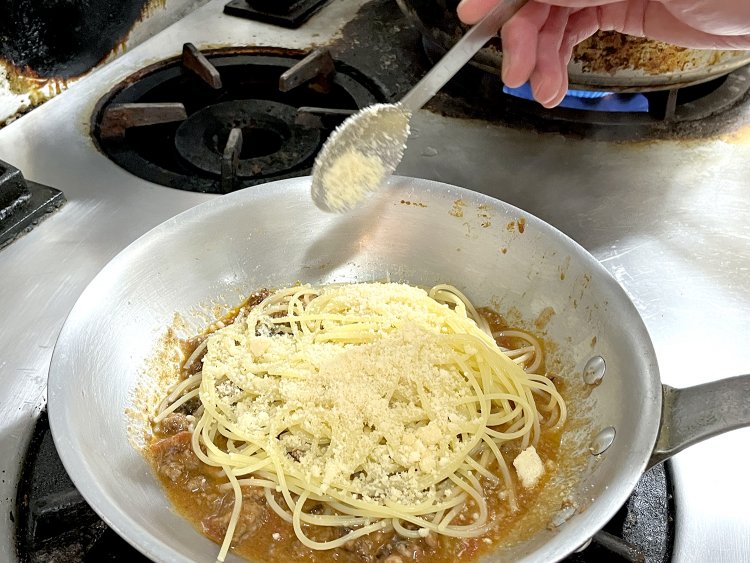 茹で上がったパスタとミートソースを炒め合わせる。このときにも粉チーズをたっぷり！