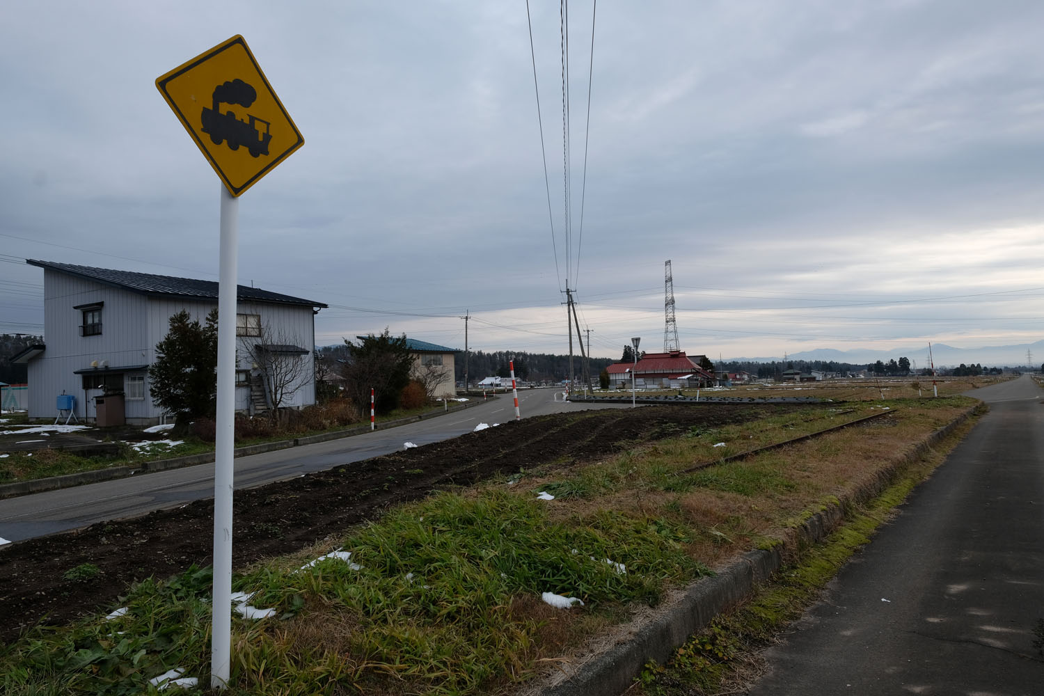 会津加納駅跡の先に突如として現れる遺構。緑地帯をよく見るとレールが残されている。踏切注意の標識はモニュメントとして設置したものと思われる。2016年12月13日撮影。