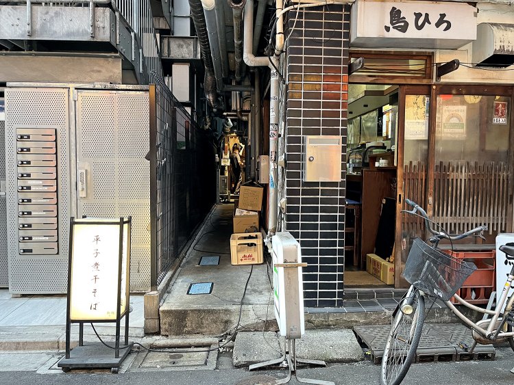 ビールケースや段ボールなどが置いてあり、店の通用口かと思っていたが。え〜、まさかココを入っていくの!?