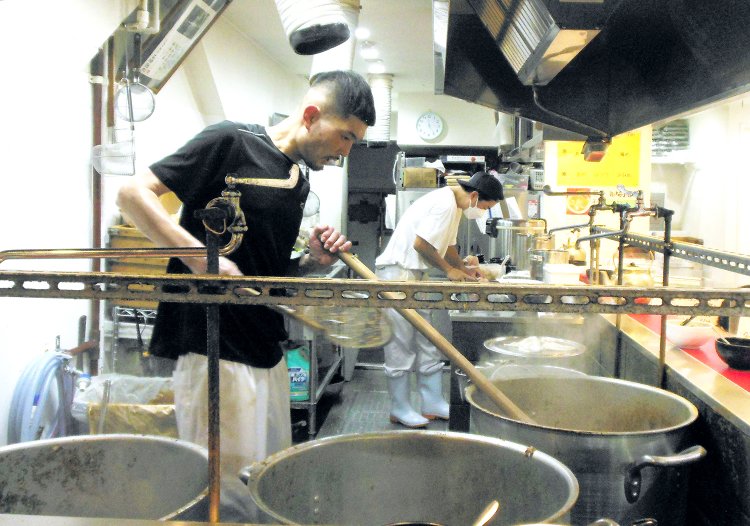 長くいヘラのような道具で大きな鍋をかき混ぜ、豚骨スープを炊く。