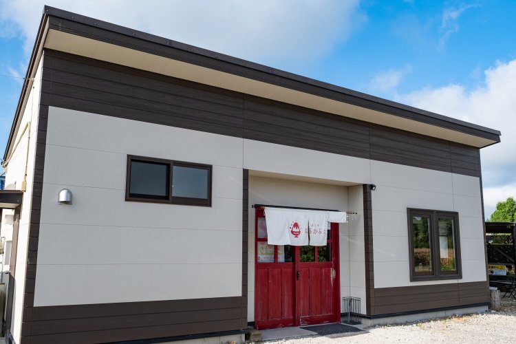 赤い引き戸と、そよ風にはためく白いのれんが印象的な店舗外観。