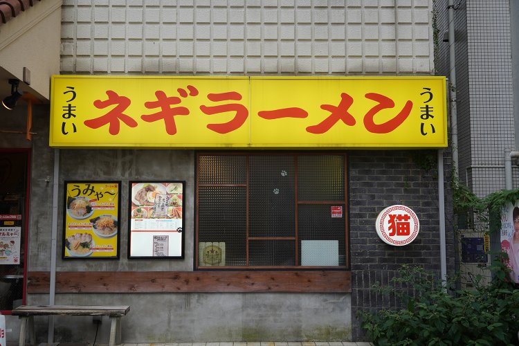 ラーメンショップの赤い看板をもじった黄色の看板。左右の「うまい」に挟まれるのは看板メニューのネギラーメン。
