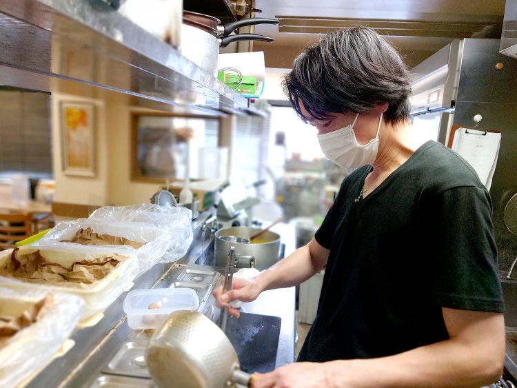 手際よくラーメンを作る大町さん。広い厨房の奥には自家製麺の要、製麺機が見える。