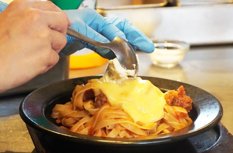 チーズソースの上に何かを乗せている……。