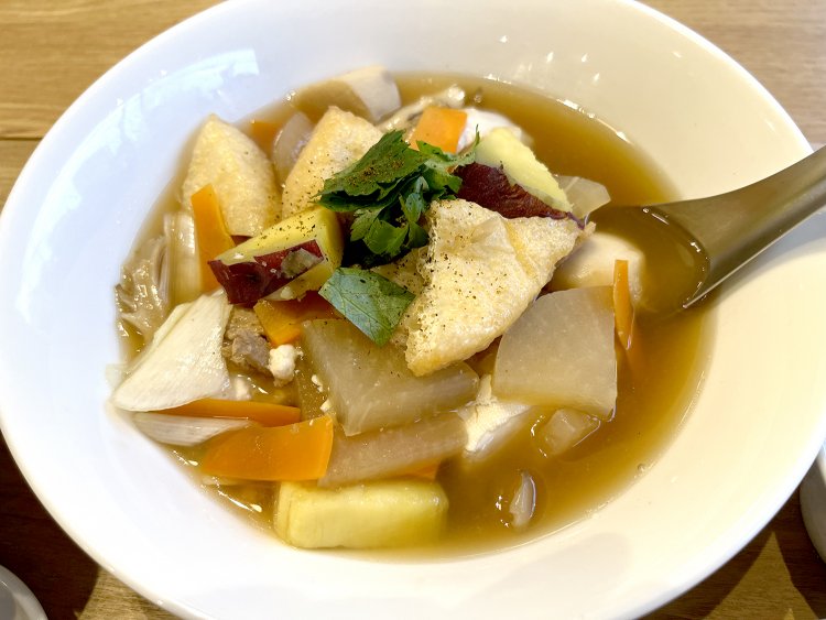 木綿豆腐、揚げ豆腐（三角揚げ）のほか、根菜を中心にした９種の具材が入る豆腐汁。いりこだしと麦味噌のやさしい風味。じんわり染みる〜。