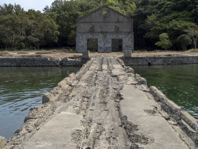 振り返ると空気圧縮ポンプ所の壁面がドンとある。桟橋の溝が線路の片分岐のようになっていて興味深い。魚雷を左右のレール？に割り当てるときの渡り線か。