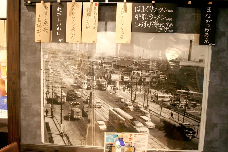 店内に飾られた品川駅前の古い写真。右が駅舎で泉岳寺方面を向いて撮影されている。写真のちょうど中央のあたりに「紀州屋果実店」の看板が見える。