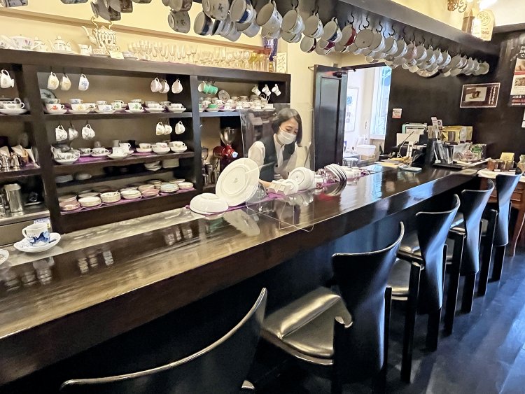 カウンター席に座ると好きなカップでコーヒーを入れてくれる。ガラスケースに入った約300年前のアンティークカップもある（使用不可）。