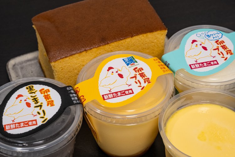 卵黄をたっぷり用い、甘さ控えめのプリンは左から黒ごまプリン、卵菓屋プリン 各250円、生クリーム入り卵菓屋プリン300円。後列はクレタマカステラ Sサイズ520円。