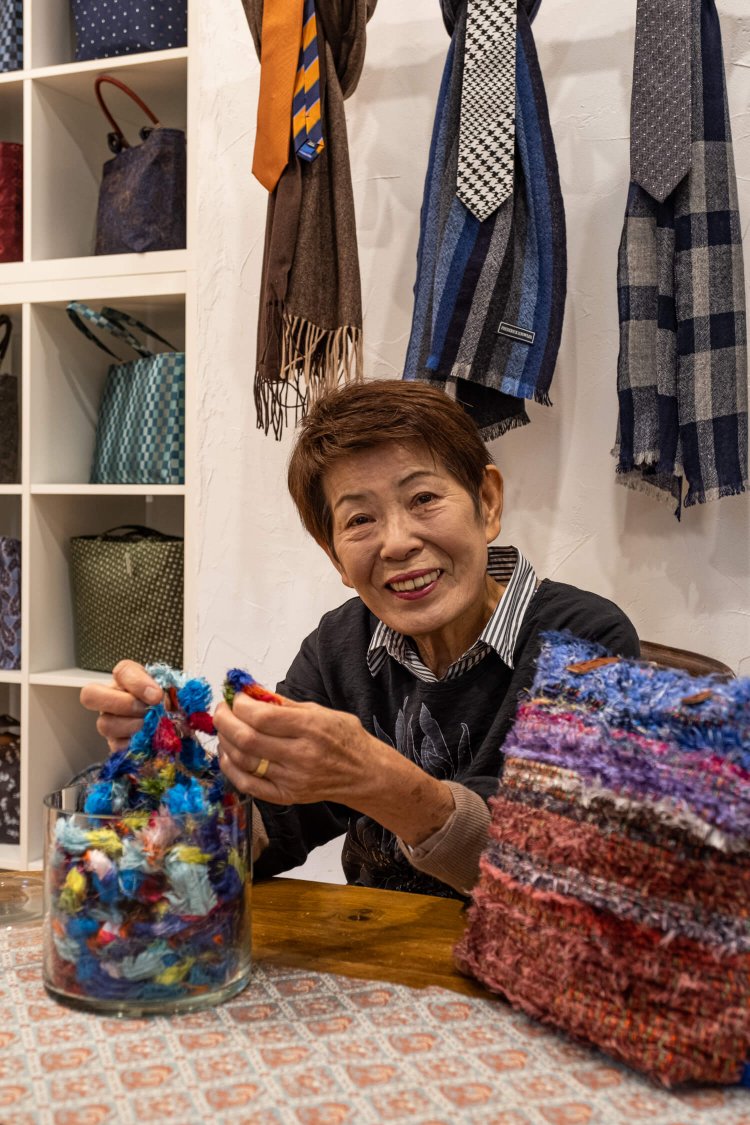 本来は廃棄されるネクタイ生地の耳（セルビッチ）を手織りした一点物のバッグ（1万5000円前後）を前にした花上淳子さん。