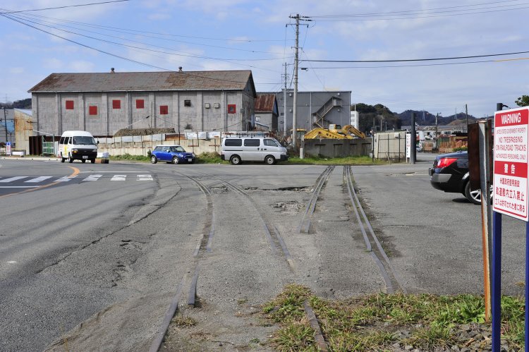 横須賀港湾合同庁舎前の廃線跡。分岐箇所はアスファルトに埋もれかけているが、レールの頭が露出していた。右手の線路はその先でプツっと途切れている。ここにも警告看板が……。