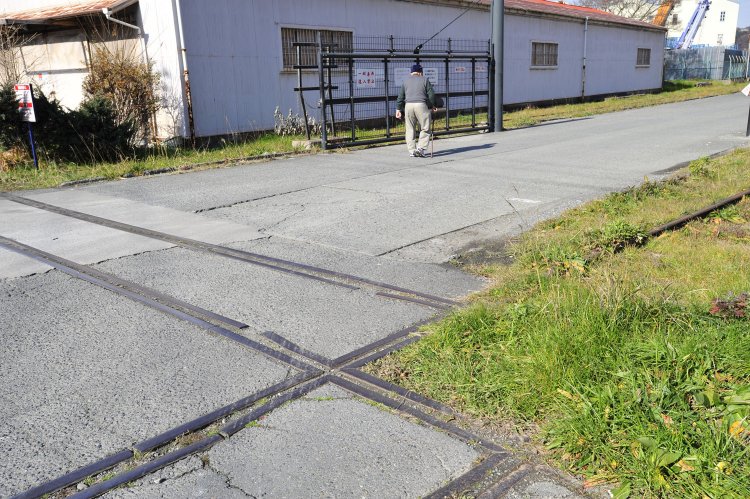 十字交差が連続するのはアミノ飼料工業へ至る専用線が複線であったからだ。複線ではあるが、両線路の間に道路がある変則的な線形である。背後のご老人は散歩中であった。