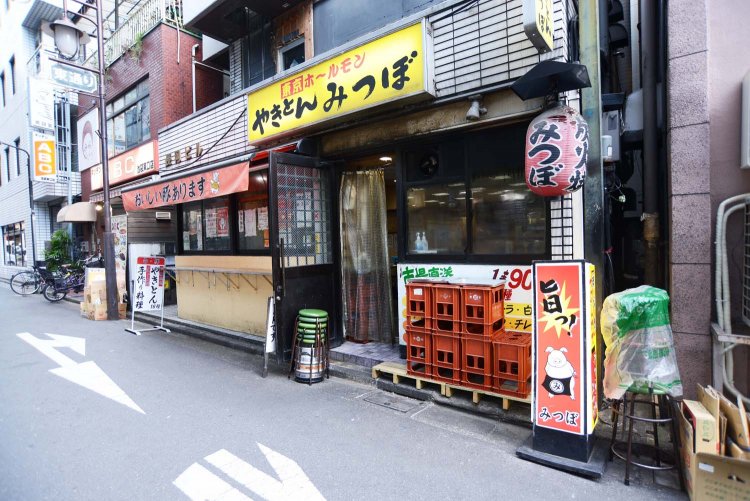 店は大通りから少し入るが黄色い看板が目印。混雑時にはオレンジ色のテントの下の屋外立ち飲みスペースも開放される。