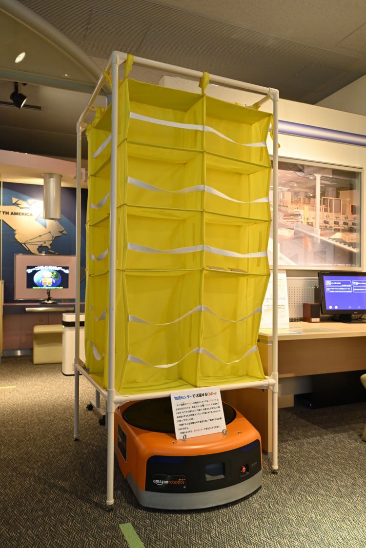 Amazonの物流センターで使われている商品を仕分けするためのロボット模型と商品棚。動画もある。