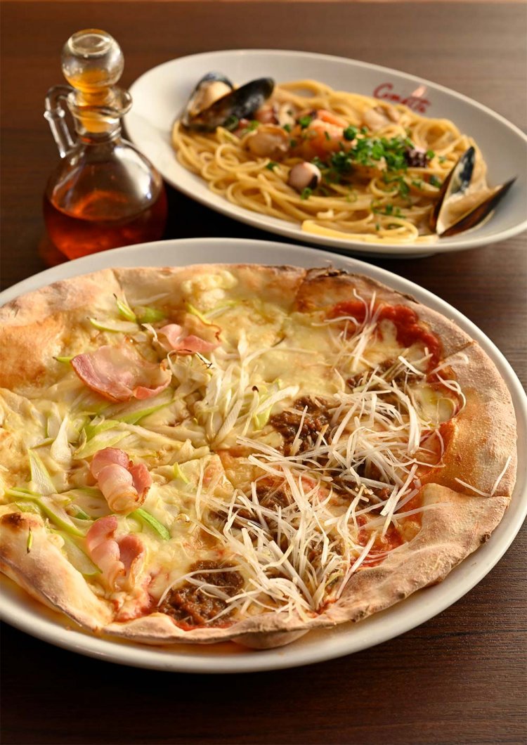 コメ・スタ18番ピッツァ1700円（手前）。海鮮もろみクリームパスタ1450円。ピザは薪を使い、石窯で焼き上がる。18番ピッツァは仕上げに醤油をかけたピザと醤油もろみを散らしたピザのハーフ＆ハーフ。