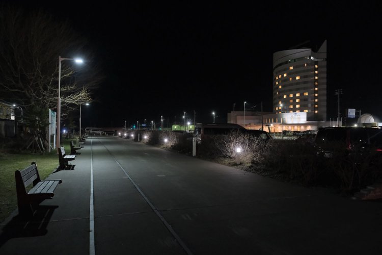 夜になると黒い線が本物の線路に見えてくるから不思議だ。北ふ頭方面へ向かう遊歩道と線路モニュメント。遊歩道は途中で途切れて駐車場となる（2023年4月18日）。