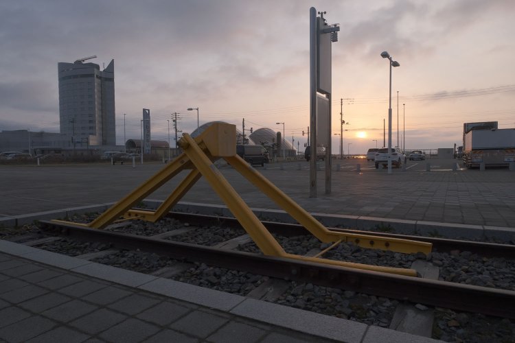朝日をバックに早朝の空気に包まれる車止め。黄色く塗装された姿は駅改良前から変わらない。バラストと枕木も敷かれている（2023年4月19日）。