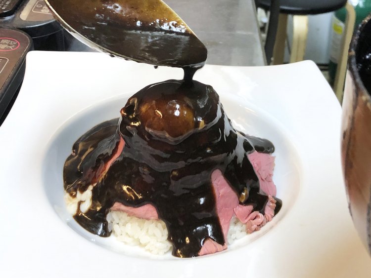 次にカレーソースを富士全体にかけていく。お皿のくぼみぎりぎりまでたっぷり。深みのある茶色に覆われた富士山が出現する。