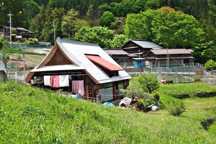 峰の中心部に立つ兜造りの民家。兜造りは奥多摩や山梨に多く見られる造り。一方、奥に見られるのは群馬県や埼玉県に多い切妻平入りの家。