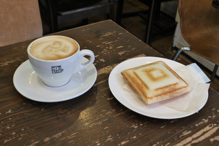 ミルクたっぷりラテ390円（写真左）と小倉のホットサンドイッチ280円（写真右）。店のロゴがあしらわれたオリジナルカップもかわいらしい。