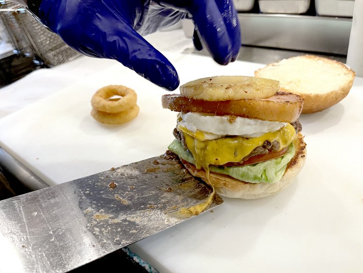 レタス、トマト、パティ、チーズ、卵、ベーコン、パイナップルときて、まだまだ乗る！　とろけたチーズが舌を出しているみたいでかわいい。